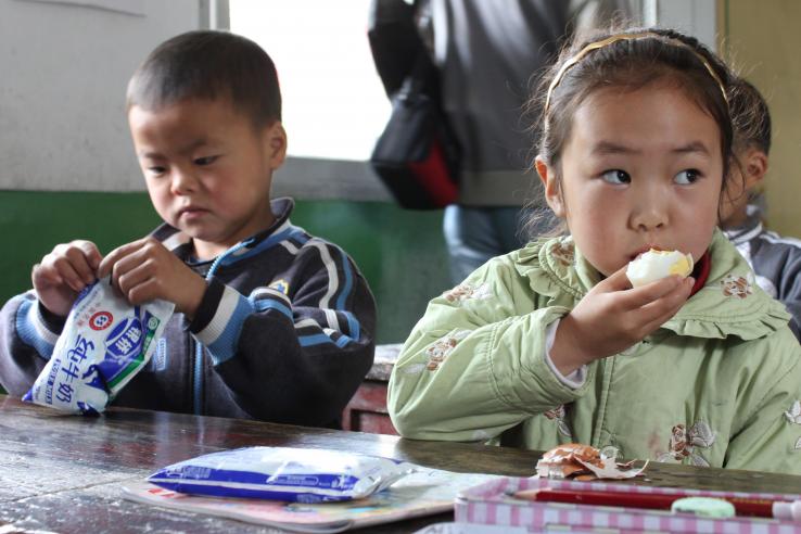 Young boy opening bag and girl eating egg