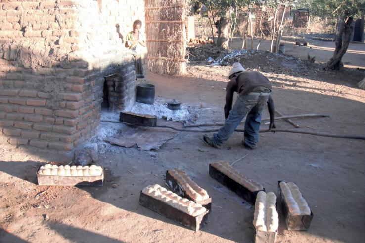 Man puts large loaf of bread into outdoor wood fired brick oven