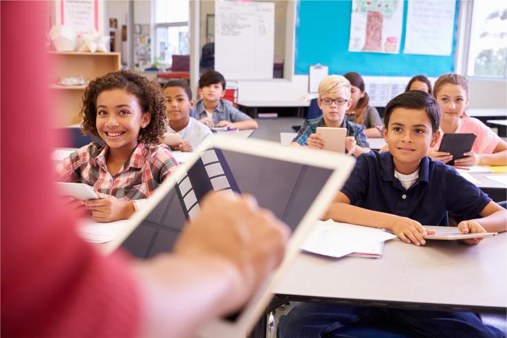 Children in a classroom looking at teacher with an iPad