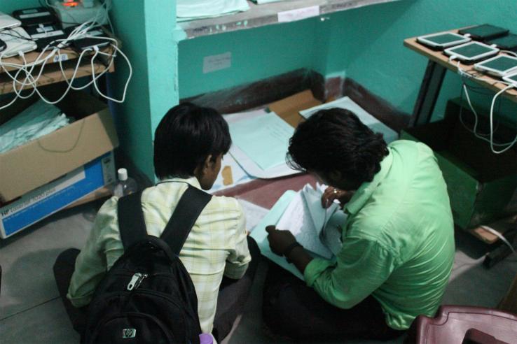 Two men sit on the ground looking at paper surveys