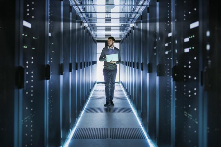 Man holding laptop walking through data center room