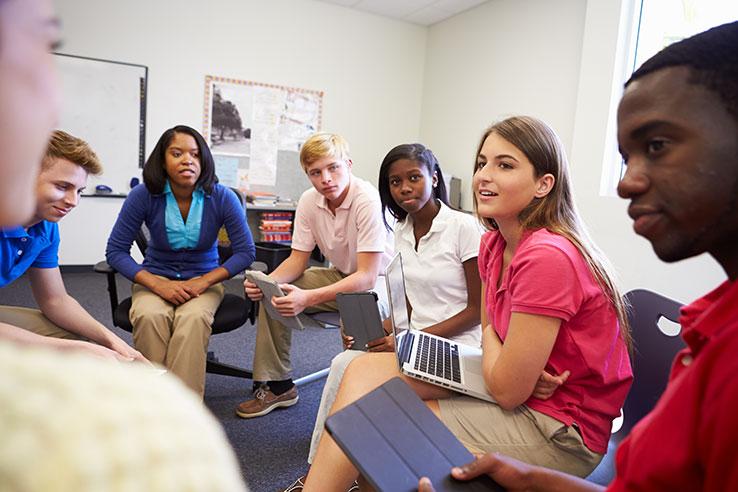 Teenagers sit in a circle in a classroom, talking.