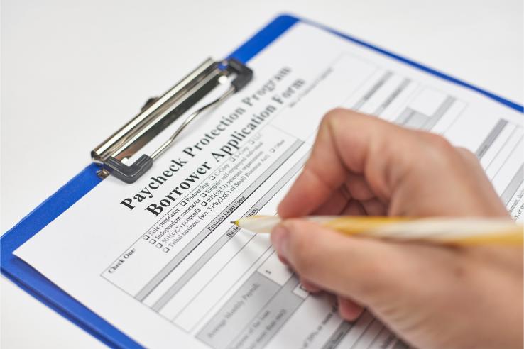 A hand fills out a PPP loan application form.