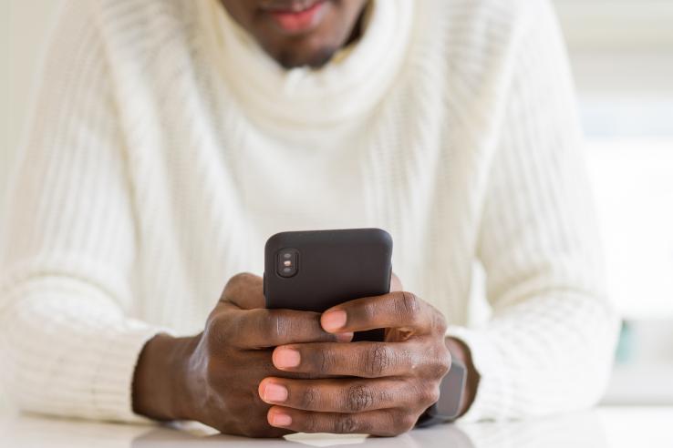 A close up image of a man holding and looking at a smartphone