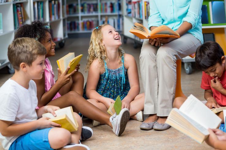 A person reads to young children sitting on the ground.