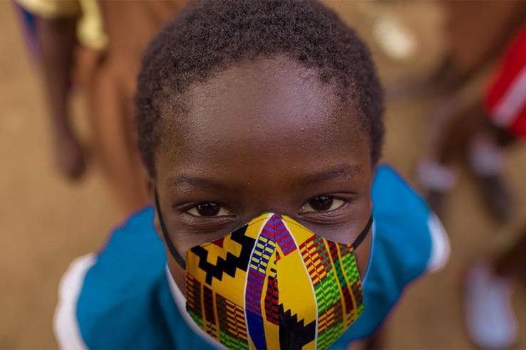 A child wearing a mask looks directly up at the camera