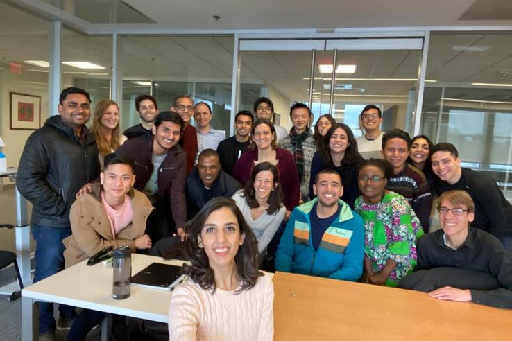 A group of DEDP master's students stand behind a table in an MIT classroom.