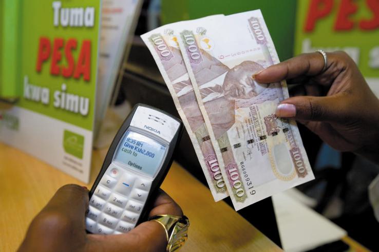 Two hands holding money and mobile phone to conduct a mobile money transfer