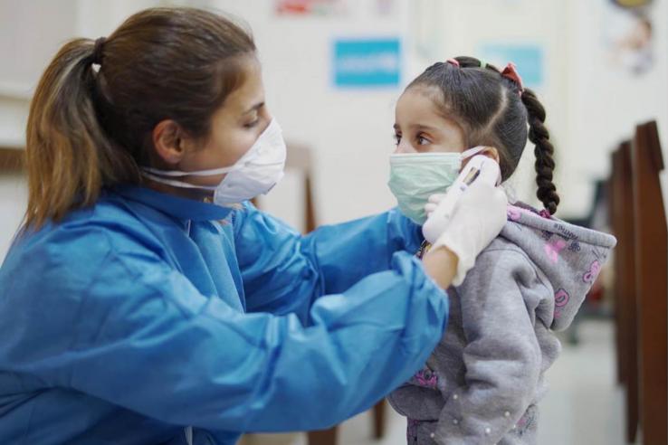 A woman with a mask on puts a mask on a young girl