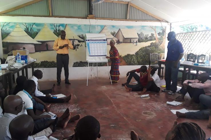 A person is speaking in front of a group of teachers in a classroom.