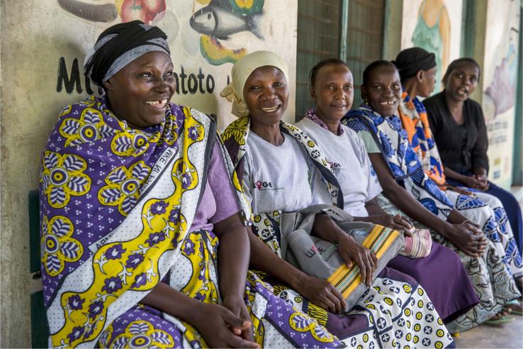 Six women sit in a row with their backs to a wall