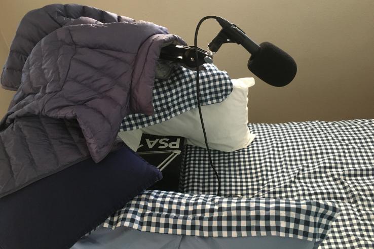 A microphone sits on top of a pile of pillows and blankets