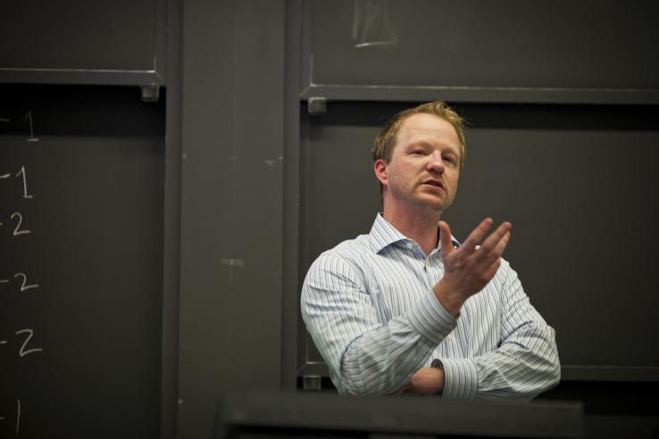 Chris Knittel lectures in front of a blackboard.