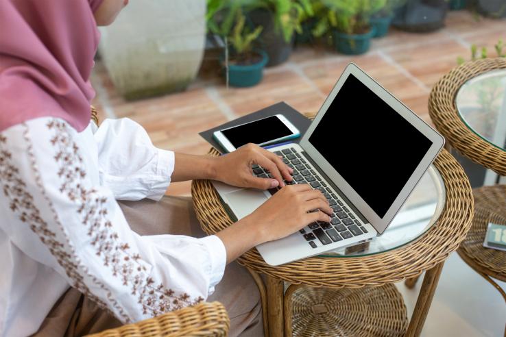 A woman wearing a hijab sits typing at a computer