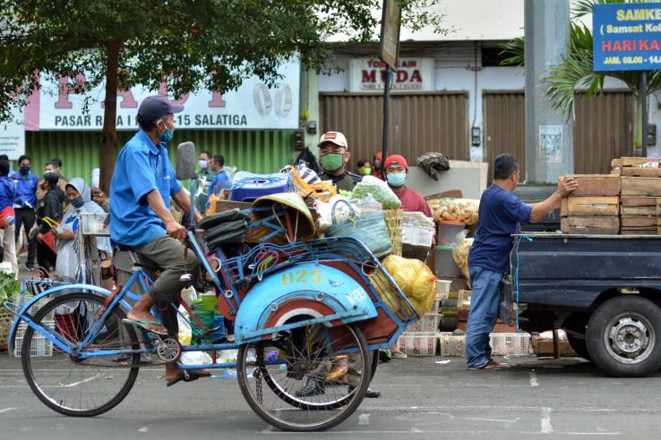 A person wearing a mask peddles a bike through an outdoor market.