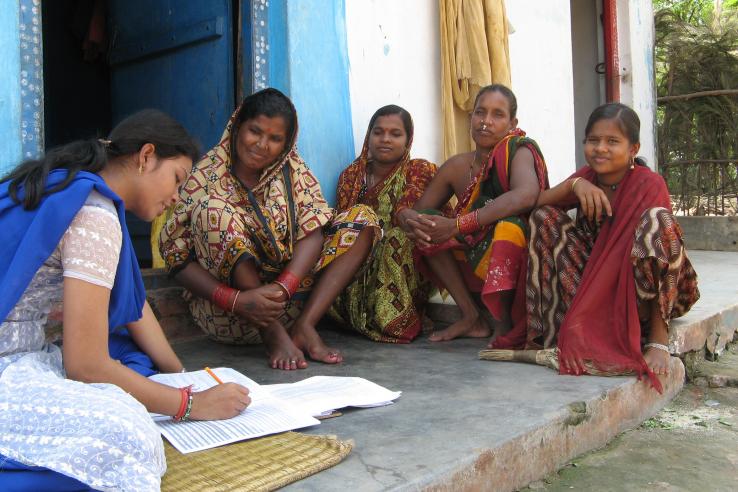 women seated around a surveyor as she notes down their responses