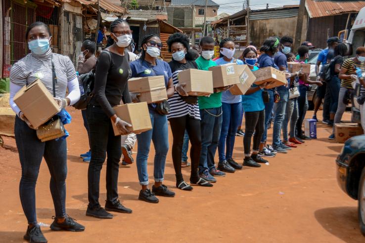 Men and women are lined up outside holding boxes containing food aid.