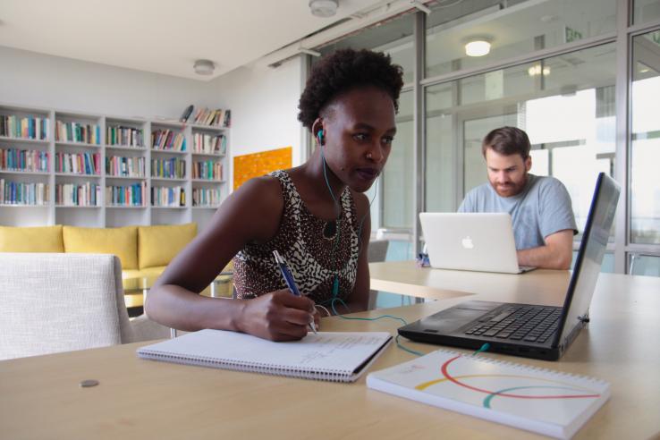 A woman sits at a desk with a notepad and laptop computer.