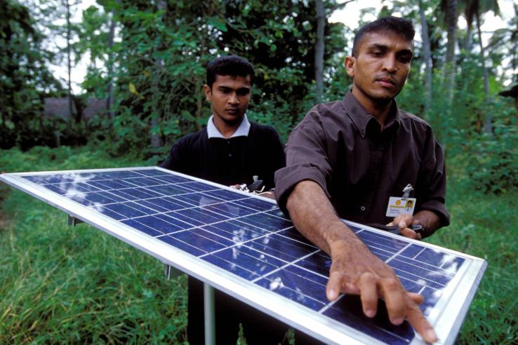 Two men work on a solar panel on used for lighting village homes in Sri Lanka