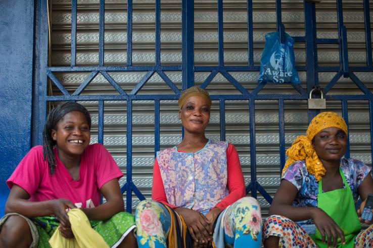 Three African women sit together and smile at the photographer.