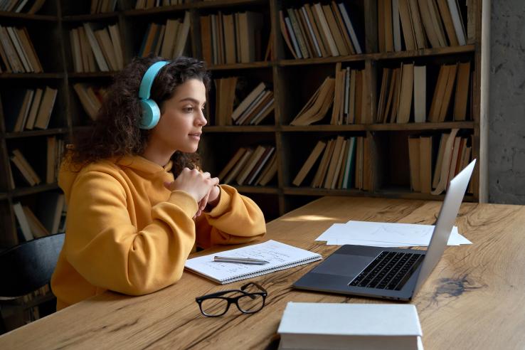 A young girl wearing headphones sits in front of a laptop with notebooks beside her