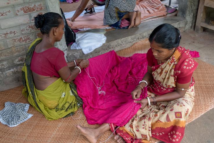 Women in Debanandapur, West Bengal, India sitting on the ground while sewing and ironing garments.