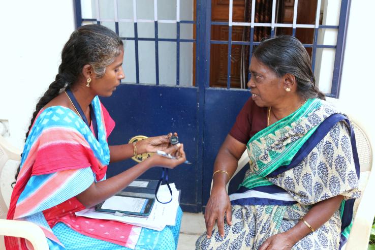 Two women sit face to face. The woman on the left holds a pedometer and is speaking to the woman on the right.