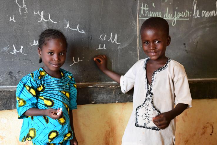 Two kindergarten children stand in front of a blackboard, smiling.
