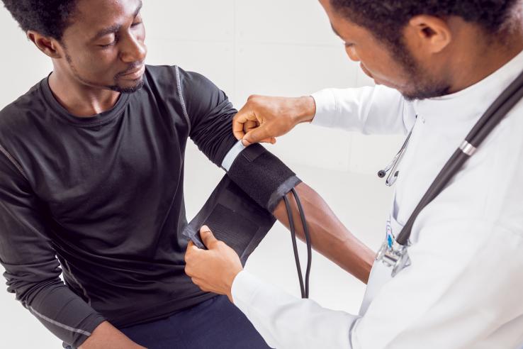 A Black doctor takes the blood pressure of a seated Black man