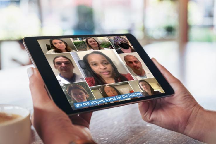 Hands hold a tablet with an image of a doctor delivering information about Covid.