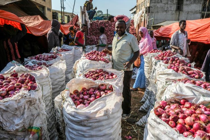 A market vendor stands in front of large sacks of onions