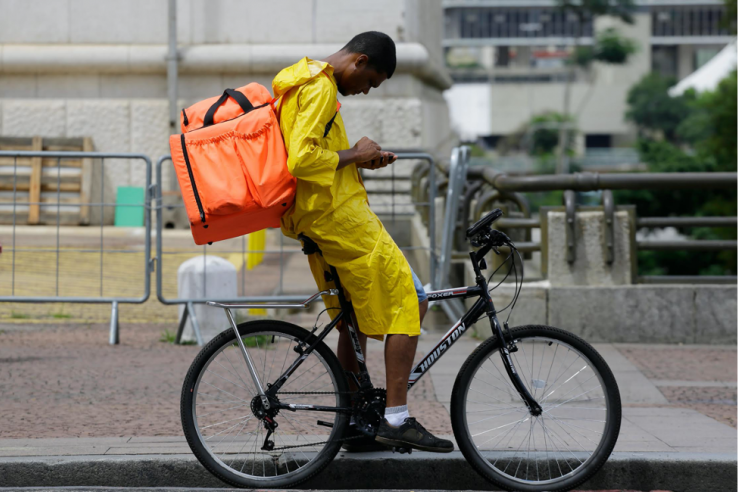 A young bike delivery person sits on his bike and checks his phone.