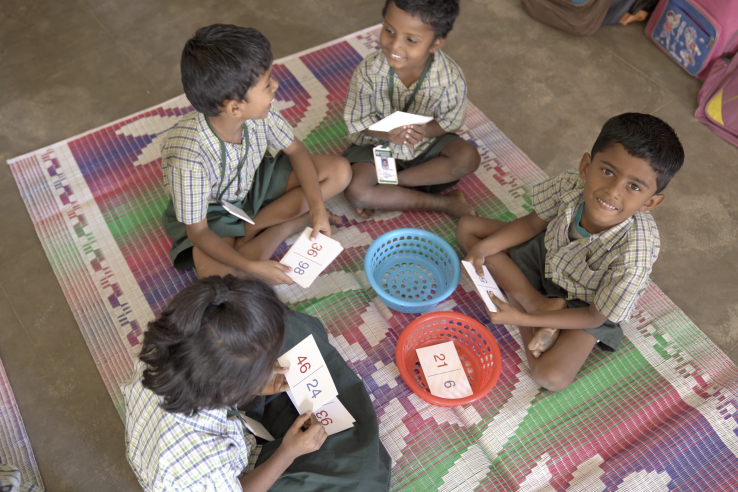 Children in an India classroom sit in a circle on the floor and play a math learning game.