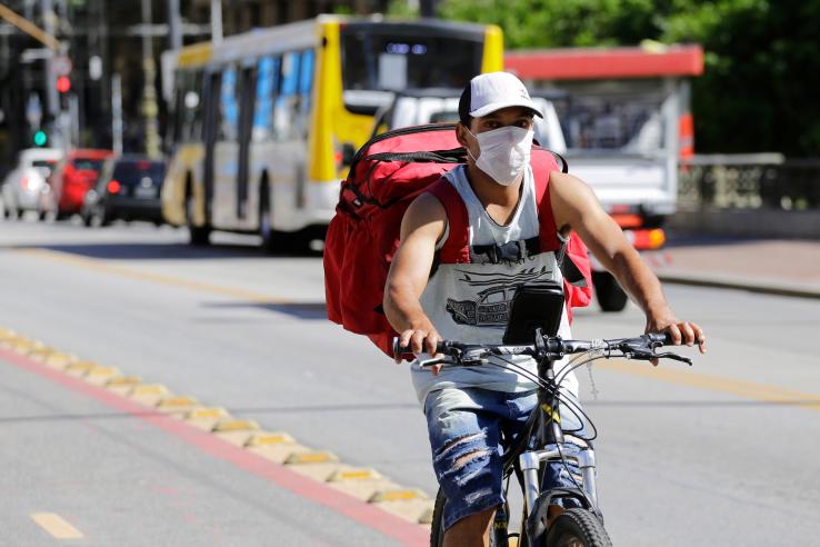A man rides a bicycle wearing a delivery backpack and a mask