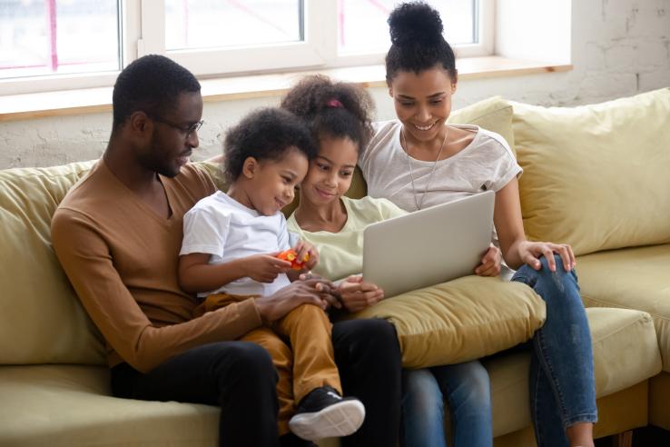 A family of four sitting on a coach looking at a laptop