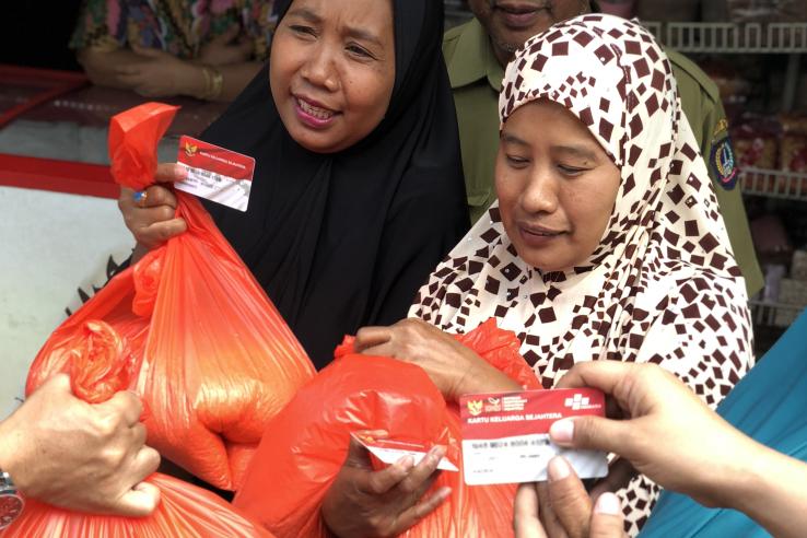 Two women hold up their Indonesian benefits card to receive bags of rice.