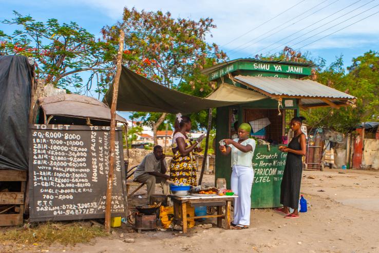 Women prepare food for sale in front of a shop in Kenya.