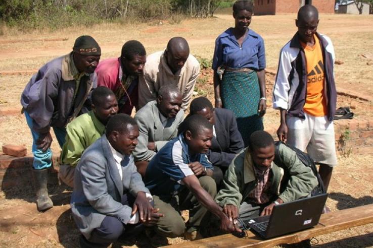 Farmers in Malawi gather around a laptop to learn about fingerprinting technology.
