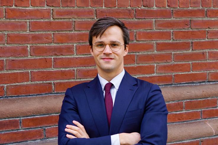 Headshot of John Tebes in a suit in front of a brick wall