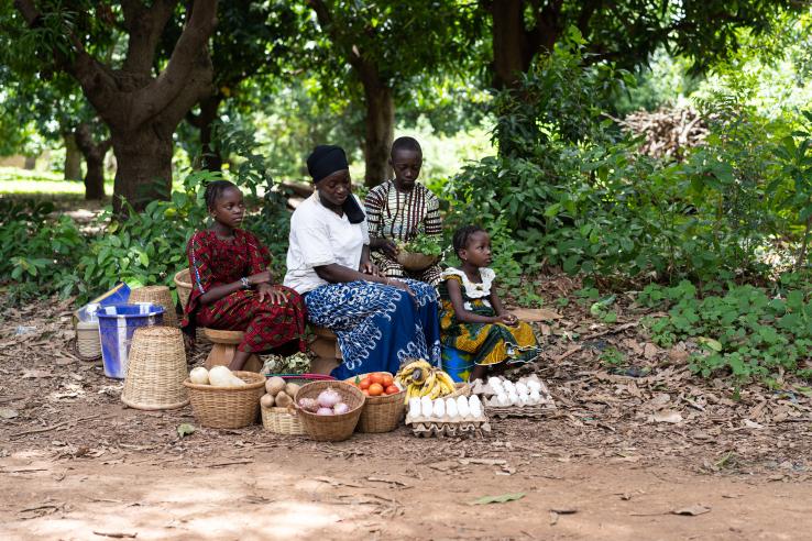 West African woman and children sitting on the edge of a dirt selling home grown produce
