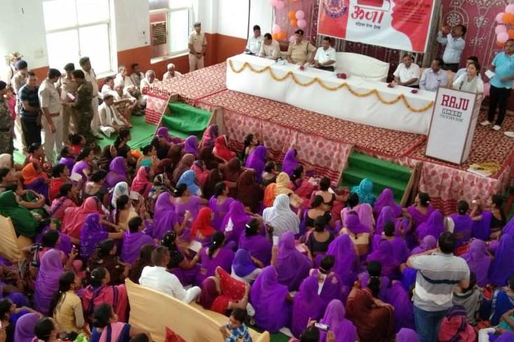 A large group of mostly women, many of whom are wearing purple, sits in front of a stage with eight people on it.