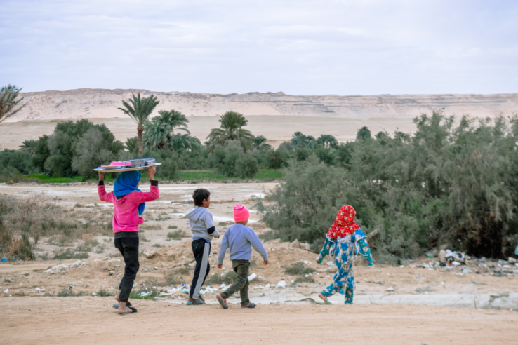 A woman carries a large tray of items on her head while walking with three young children in Egypt. Ahmed Emad © UNICEF/UN0639390/Emad