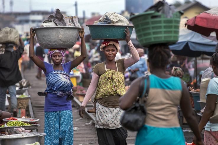 Women wearing colorful clothes carry goods in baskets on their heads in a market in Accra, Ghana. 