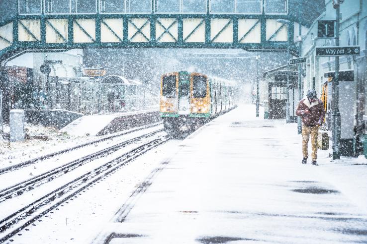 Train pulls in to London Road station while man walks on platform in heavy snow