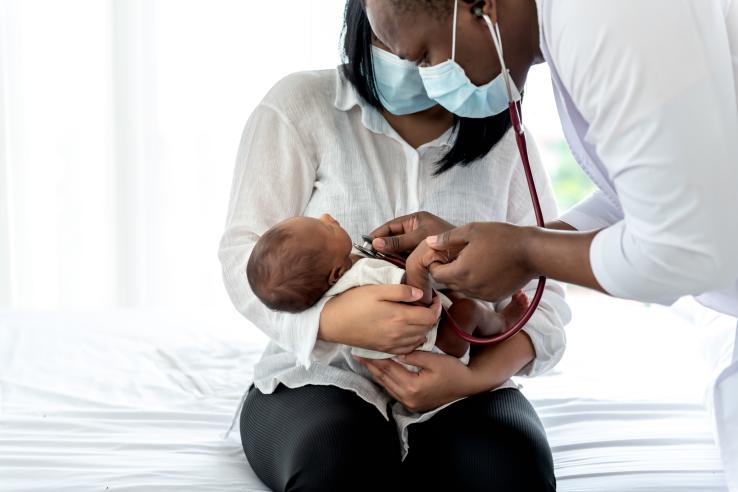 Doctor checks baby's heartbeat, held by mother. 