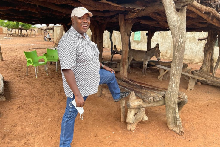 Robert Darko Osei stands under a wood structure with a mule in the background.