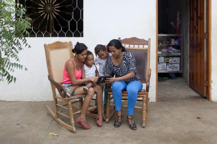 Una líder de proyecto le muestra a su vecina una herramienta de educación financiera para personas receptoras de transferencias monetarias condicionadas en Colombia.