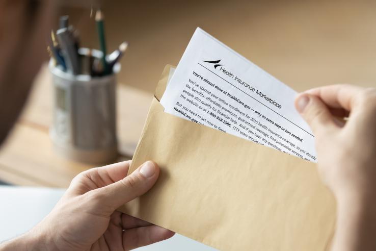 Person opening opening mail with letter containing text "Health Insurance Marketplace: You're almost done at Healthcare.gov..."