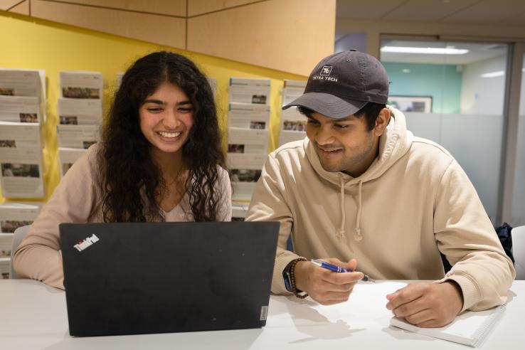 Two students sitting at a table looking at a laptop 