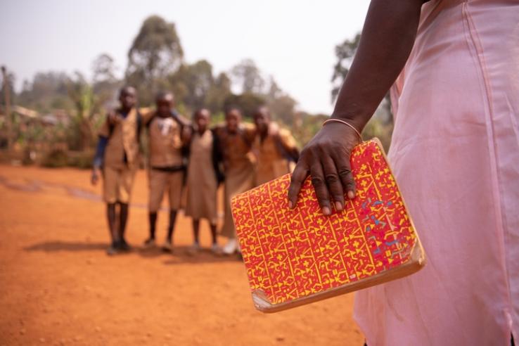 An African teacher holds a book while approaching her students.